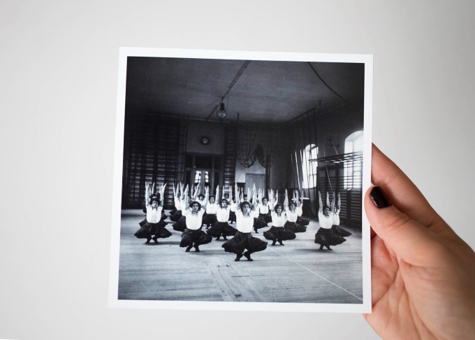 Någon håller upp ett svartvitt foto av kvinnliga linggymnaster i en gymnastiksal. Gymnsterna sitter på huk och sträcker upp armarna ovanför huvudet.