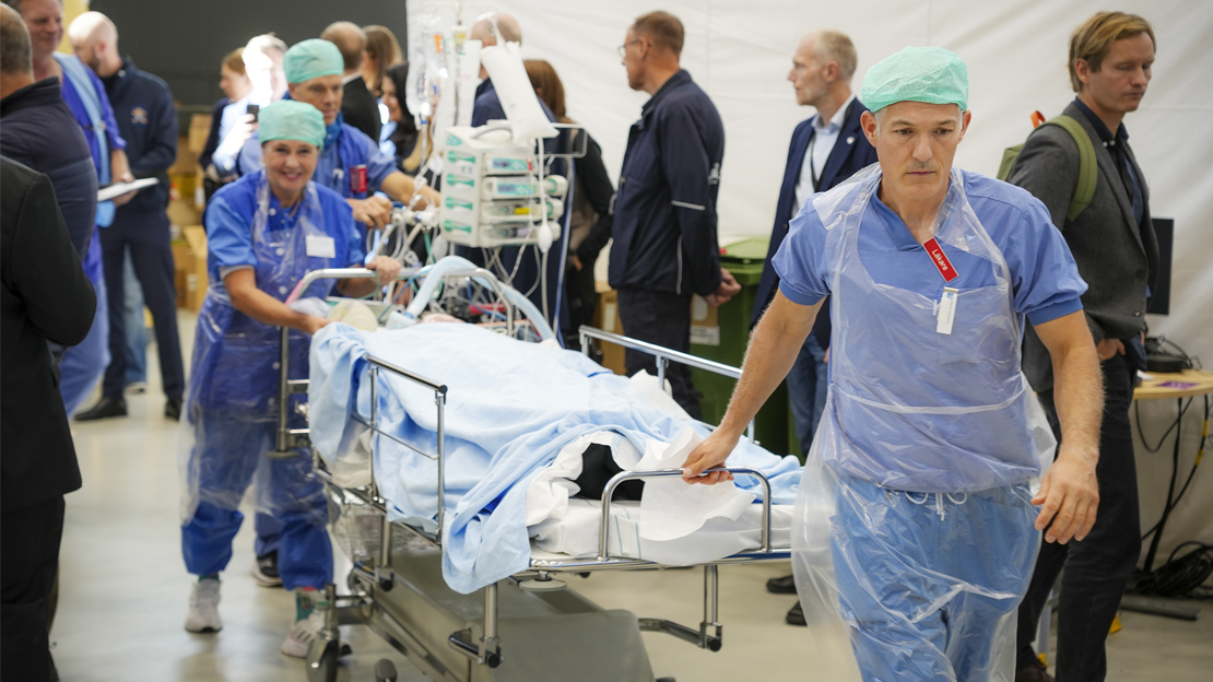 Två läkare i sjukvårdens blåa kläder drar en bår med hjul. På bården ligger en patient.