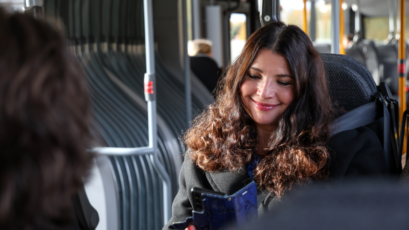 En kvinna som sitter på en buss och kollar på sin mobil.
