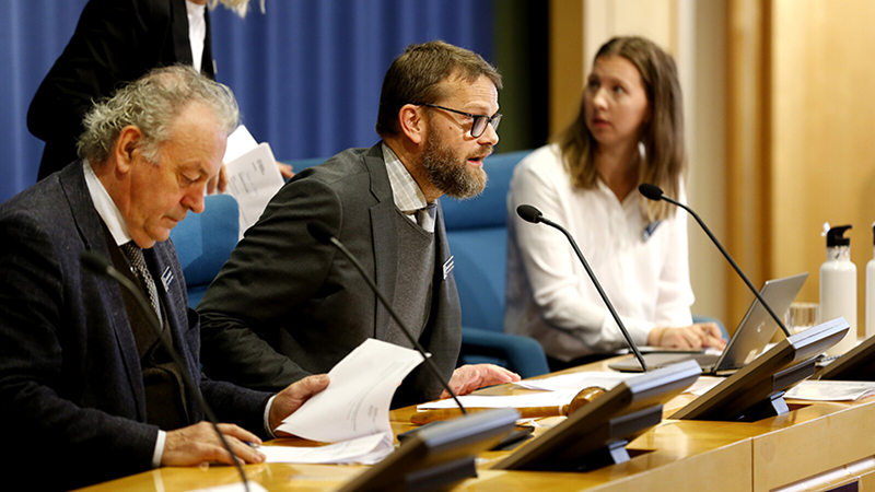 Tre personer vid skrivbord på podium