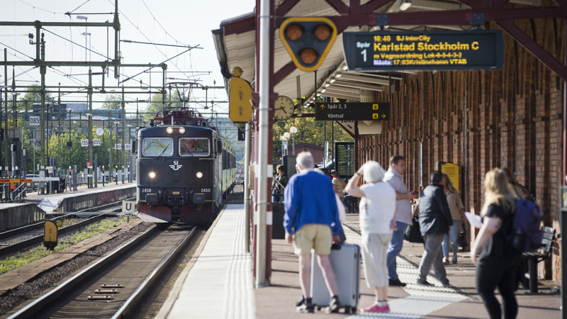 Grupp av personer på perrong där tåget just anländer. På informationstavla står det Karlstad Stockholm C.