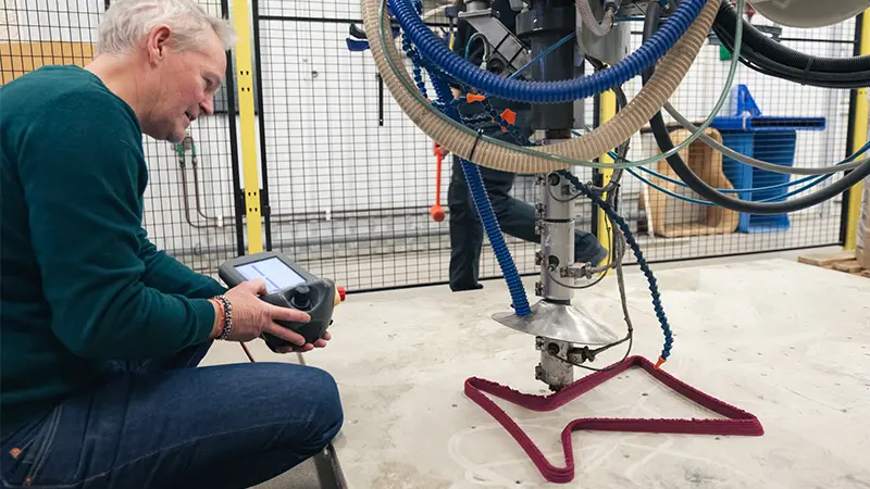  A man operates a machine that shapes a horizontal pink figure.