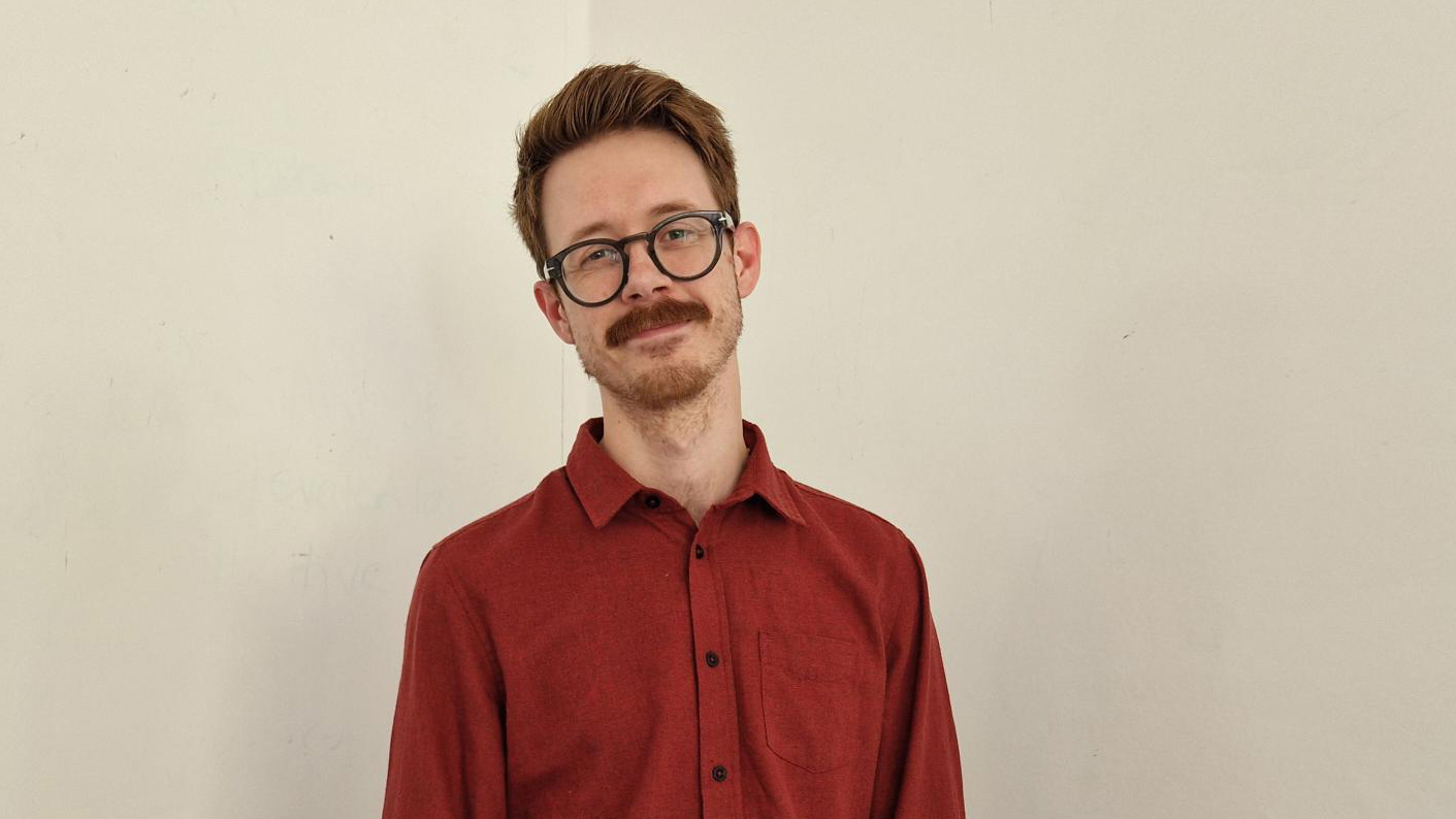 En man med mustasch och glasögon tittar in i kameran.
