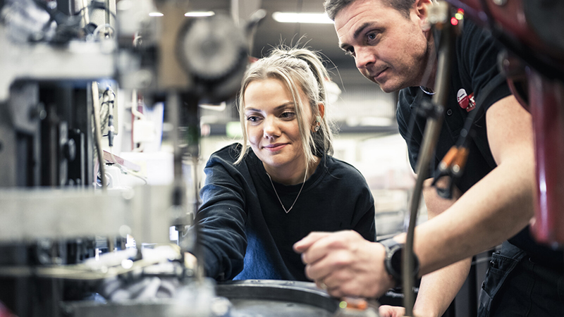 En kvinna och man står vid en industrimaskin.