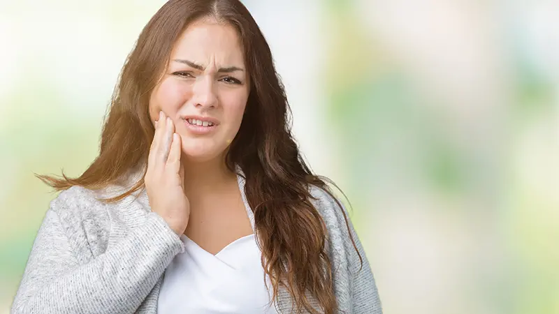 Kvinna håller handen vid kinden i samband med smärta i käken