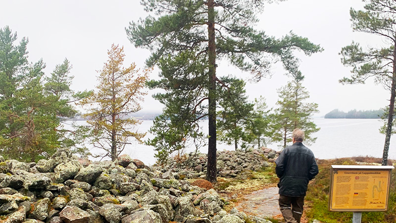 En person går förbi ett stenröse mot sjön Fryken.