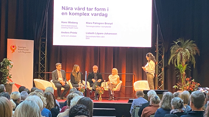 Grupp personer som sitter på en scen i paneldebatt.