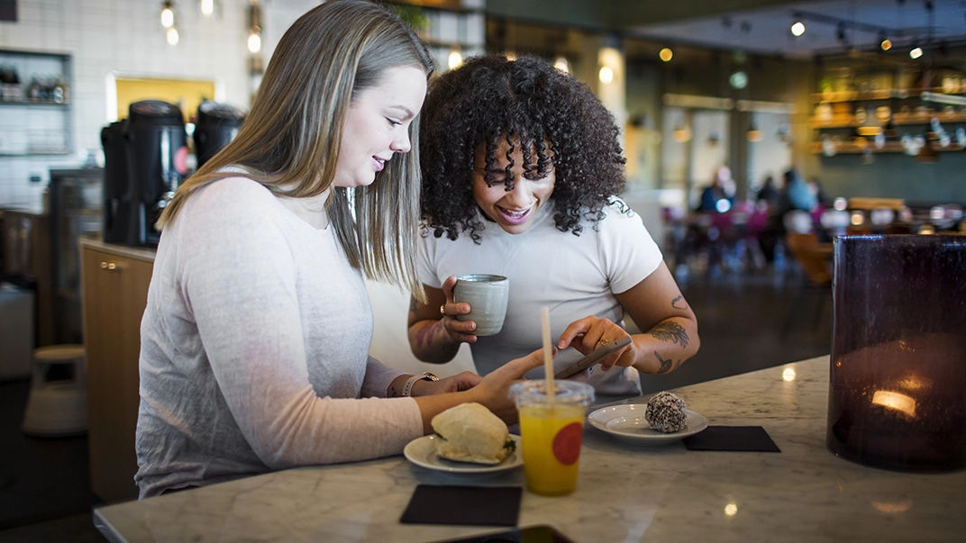 Två unga tjejer fikar på café. 