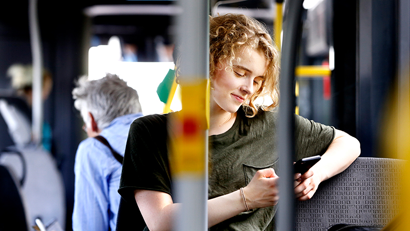 Ung person som sitter på bussen och kollar på din mobil