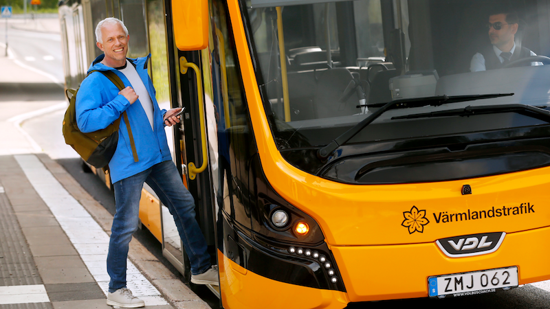 Man i blå jacka kliver på en gul buss. 