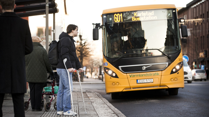 Man med kryckor som väntar på bussen på hållplatsen.
