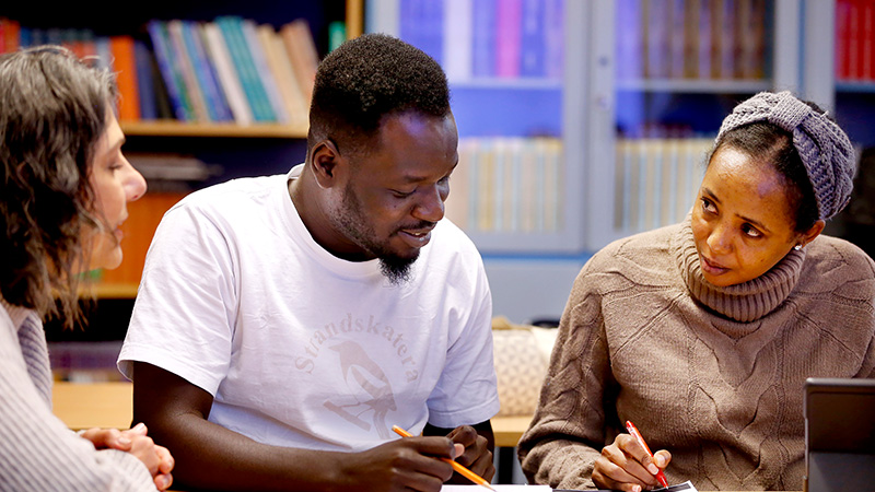 Tre personer sitter och studerar vid ett bord. 