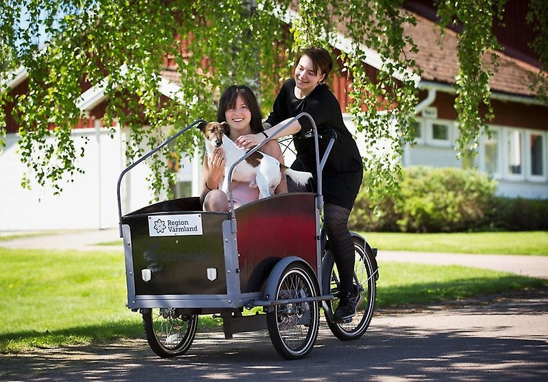 Två glada kursdeltagare och en hund i en lådcykel